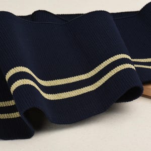 May include: Navy blue ribbed knit fabric with two gold stripes. This fabric is perfect for adding a touch of nautical style to your sewing projects.