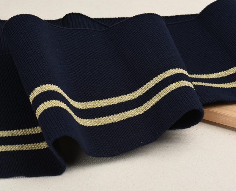 May include: Navy blue ribbed knit fabric with two gold stripes. This fabric is perfect for adding a touch of nautical style to your sewing projects.