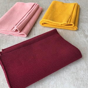 May include: Three rolls of ribbed knit fabric in pink, yellow, and burgundy.