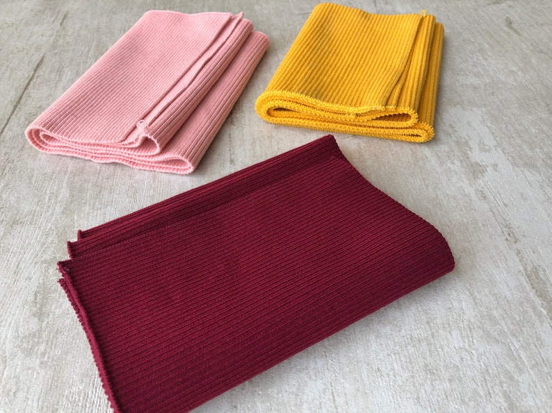 May include: Three rolls of ribbed knit fabric in pink, yellow, and burgundy.