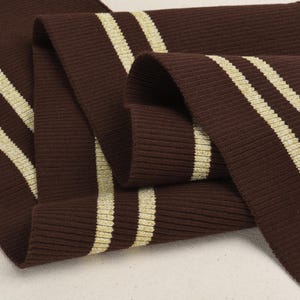 May include: Brown ribbed knit fabric with two gold stripes. The fabric is folded in half and the stripes are visible on both sides.
