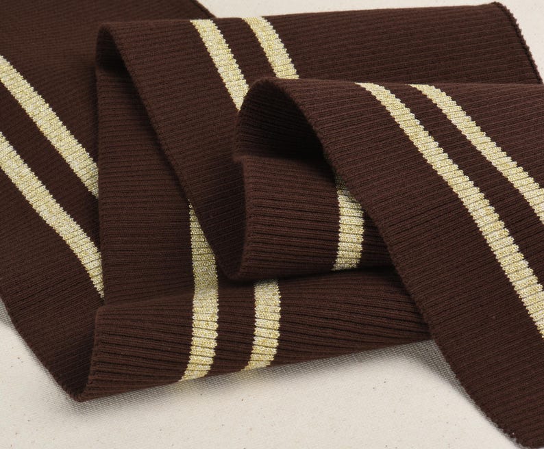 May include: Brown ribbed knit fabric with two gold stripes. The fabric is folded in half and the stripes are visible on both sides.