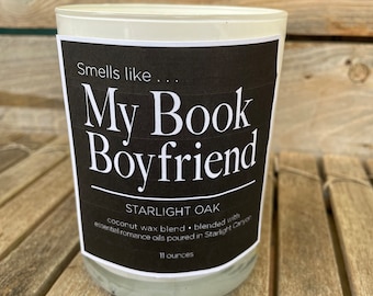 May include: A white candle jar with a black label that reads "Smells like... My Book Boyfriend" and "STARLIGHT OAK coconut wax blend • blended with essential romance oils poured in Starlight Canyon 11 ounces".