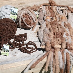 May include: Three balls of yarn in brown, beige, and gray colors, along with a wall hanging made of yarn in brown and beige colors. The wall hanging is shaped like an owl with two wooden eyes.