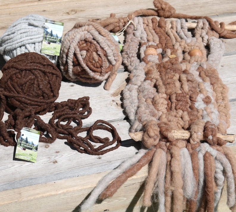 May include: Three balls of yarn in brown, beige, and gray colors, along with a wall hanging made of yarn in brown and beige colors. The wall hanging is shaped like an owl with two wooden eyes.