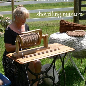 May include: A woman sits at a wooden table with a spinning wheel, winding yarn. The table is a repurposed sewing machine base. The caption reads "when I'm not shovelling manure!"