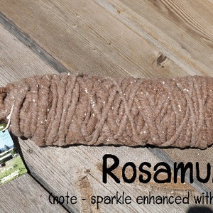 May include: A brown yarn with a sparkly finish, rolled up and tied with a white string. The yarn is labeled "Rosamund" and has a note that says "sparkle enhanced with flash".