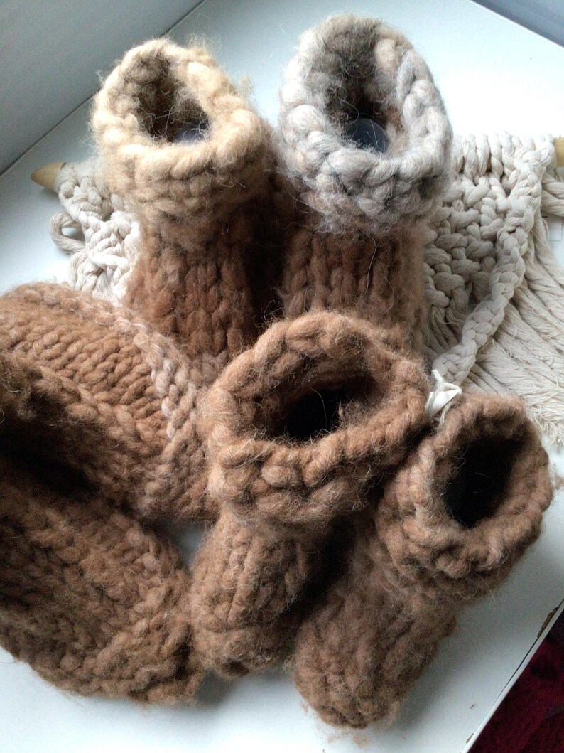 May include: A collection of chunky knit booties in various shades of brown and beige. The footwear features a thick, textured yarn construction with a high-top design and a visible ribbed cuff. The items are arranged together in a cluster.