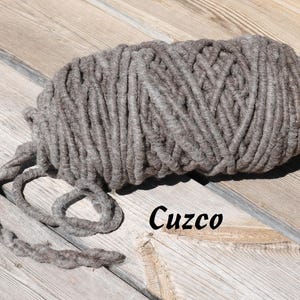 May include: A close-up of a thick, gray yarn skein, with the word "Cuzco" written on the wooden surface below it.