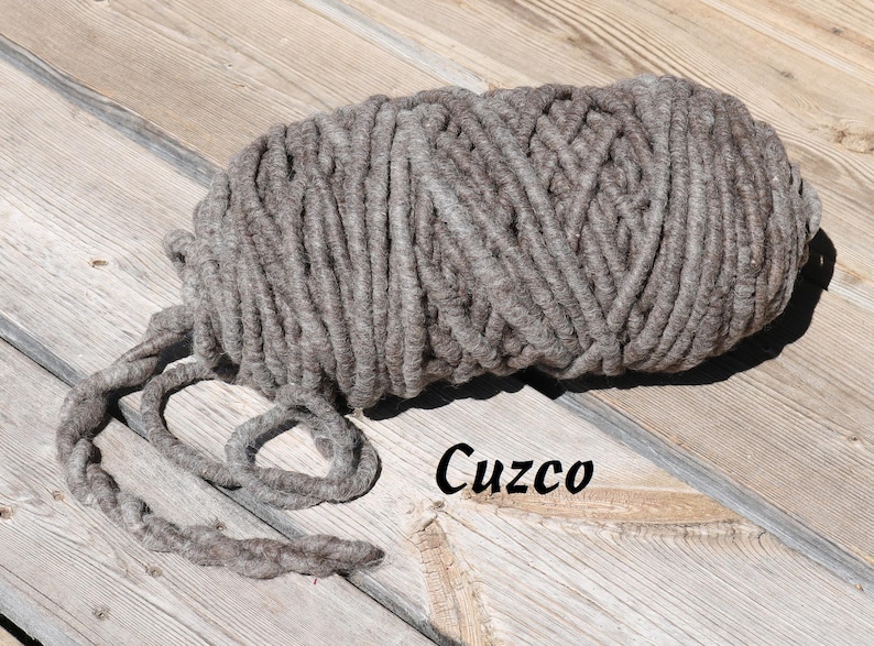 May include: A close-up of a thick, gray yarn skein, with the word "Cuzco" written on the wooden surface below it.