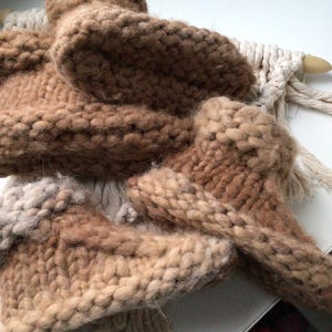 May include: A pair of chunky knit slippers in varying shades of brown and tan, featuring a thick, textured yarn construction with a visible stitch pattern. The slippers are arranged in a stack, showcasing the soft, fuzzy appearance of the wool.