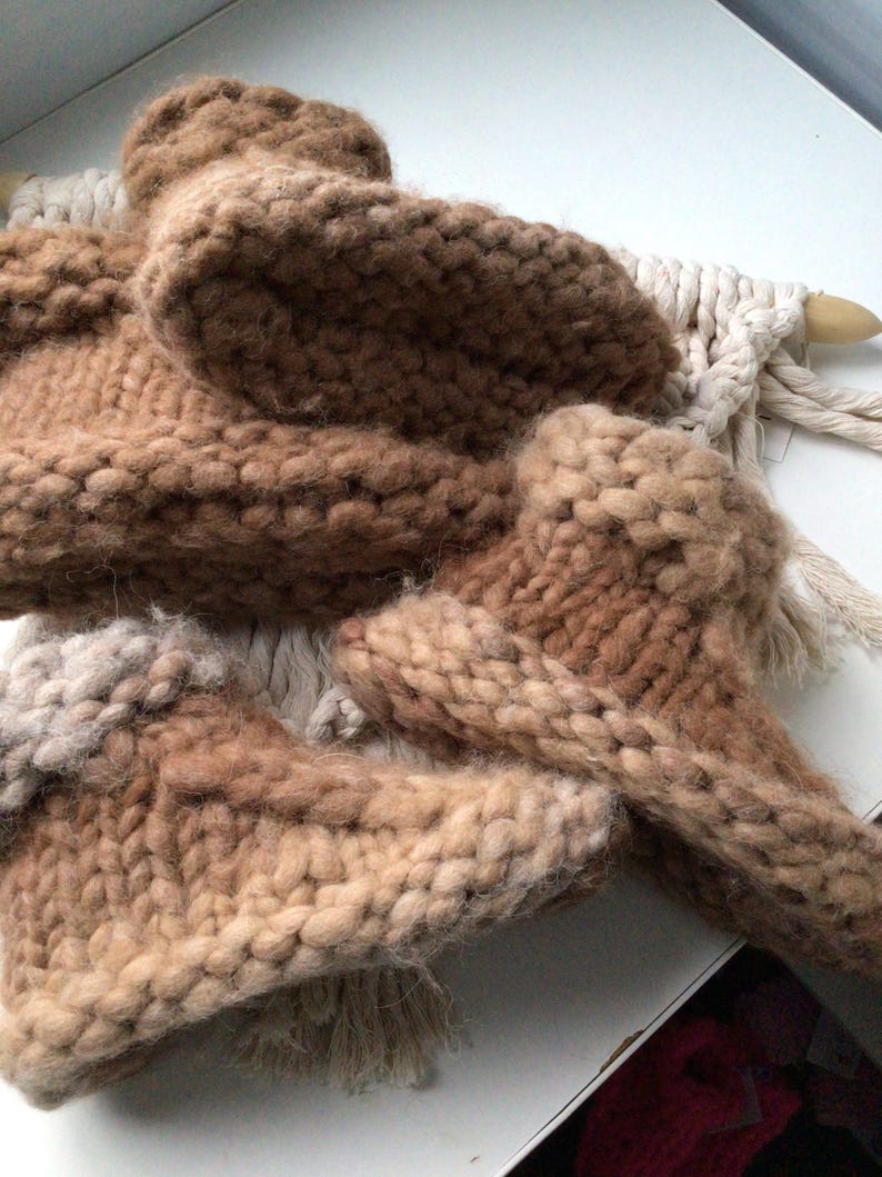May include: A pair of chunky knit slippers in varying shades of brown and tan, featuring a thick, textured yarn construction with a visible stitch pattern. The slippers are arranged in a stack, showcasing the soft, fuzzy appearance of the wool.