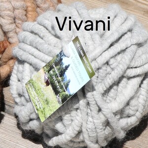 May include: A ball of light gray chunky yarn with a tag labeled Vivani and The Llama Sanctuary Llama Safari & Guided Tours. The yarn is thick and textured, featuring a soft, fibrous appearance. A portion of a brown yarn ball is visible on the left.