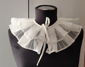 May include: White lace collar with a ruffled design and a tie at the back.