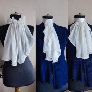 May include: Three white ruffled fabric neck collars on mannequins wearing blue sweaters. The collars are made of a sheer, lightweight fabric and have a gathered, ruffled design.