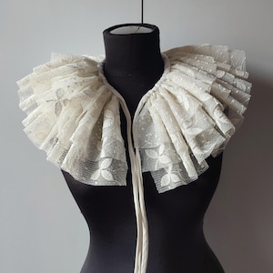 Peut inclure: Un col en dentelle blanche avec un design à volants. Le col est noué avec un ruban blanc.