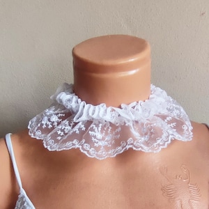 May include: White lace choker with a ruffled edge. The choker is made of delicate lace and has a soft, feminine look.