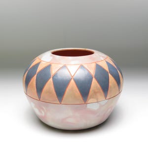 Könnte beinhalten: Eine runde Keramikvase mit einem geometrischen Muster aus schwarzen und orangefarbenen Diamanten. Die Vase hat eine hellrosa und weiße Glasur.