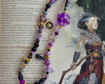 May include: A purple and gold beaded necklace with a purple 20-sided die charm and a gold sun charm. The necklace is on a book with text about warlocks in a fantasy role-playing game.