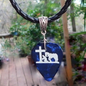 May include: A blue guitar pick necklace with a silver chain and a white silhouette of a person kneeling before a cross and a horse.