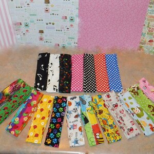 May include: A selection of patterned fabric strips, featuring designs like musical notes, polka dots, and flowers. The strips are fanned out, displaying a range of colours and patterns, ideal for crafting projects.