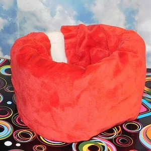May include: A red plush donut-shaped pet bed with a white trim. The bed is sitting on a black and white background with colorful circles.