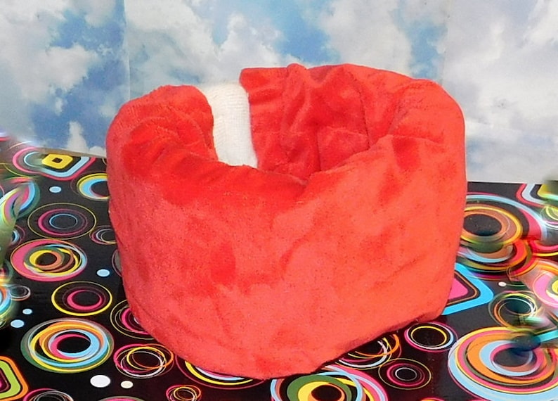 May include: A red plush donut-shaped pet bed with a white trim. The bed is sitting on a black and white background with colorful circles.