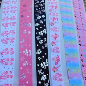 May include: Assortment of pink, white, and black ribbon with various designs. The designs include ballet shoes, butterflies, flowers, and fairies.