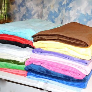 May include: A stack of 10 plush blankets in various colors, including light blue, red, black, gray, white, green, pink, and blue. The blankets are folded and stacked on a white surface.
