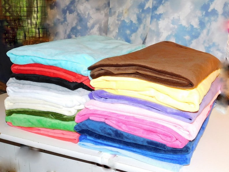 May include: A stack of 10 plush blankets in various colors, including light blue, red, black, gray, white, green, pink, and blue. The blankets are folded and stacked on a white surface.