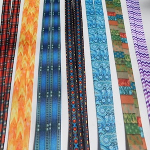 May include: Assortment of eight different patterned ribbon trims. The ribbons are all 1 inch wide and feature various colors and designs, including red, orange, blue, green, and purple.