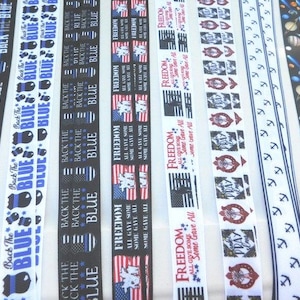 May include: Assortment of colourful ribbon with various patriotic and themed designs. The ribbons feature text such as "Back the Blue", "Freedom", and "All Gave Some, Some Gave All".