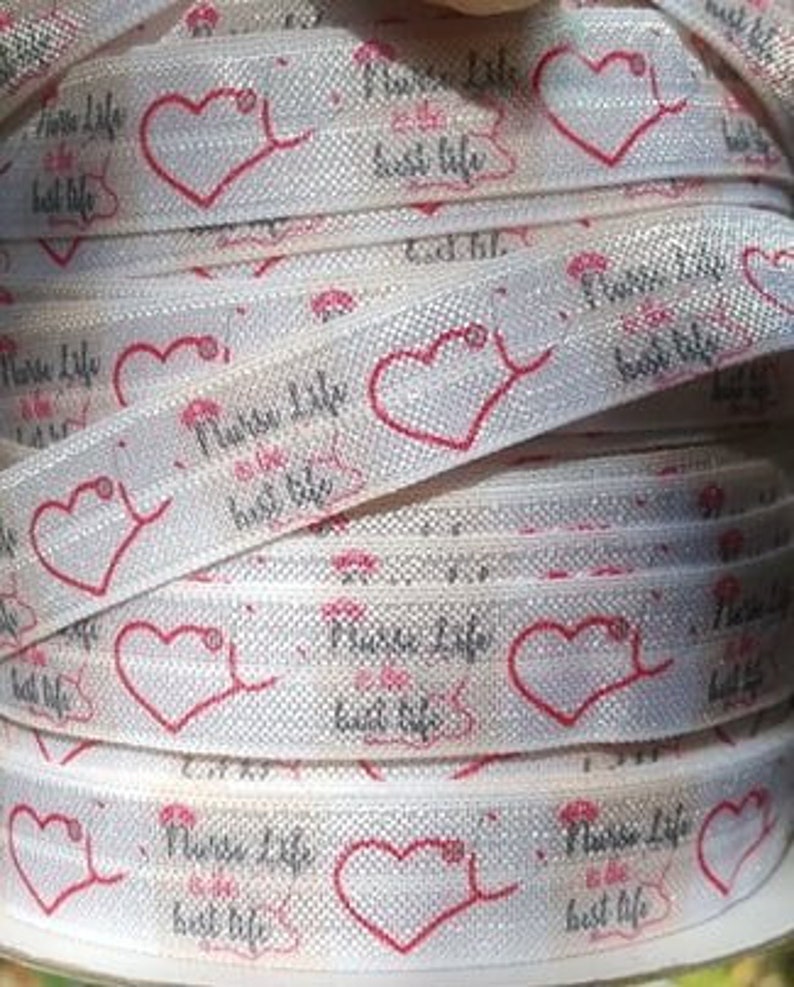 May include: White elastic hair tie with a repeating pattern of pink hearts and the text "Nurse Life Best Life".