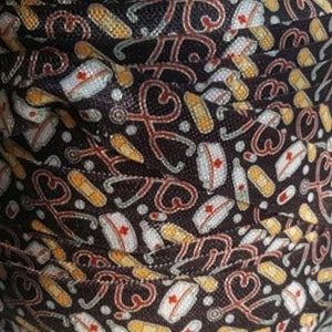 May include: Black and white fabric with a repeating pattern of medical symbols, including stethoscopes, bandages, and nurse hats. The fabric is rolled up and the pattern is visible on multiple layers.
