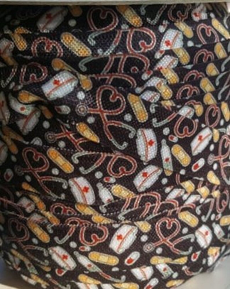 May include: Black and white fabric with a repeating pattern of medical symbols, including stethoscopes, bandages, and nurse hats. The fabric is rolled up and the pattern is visible on multiple layers.