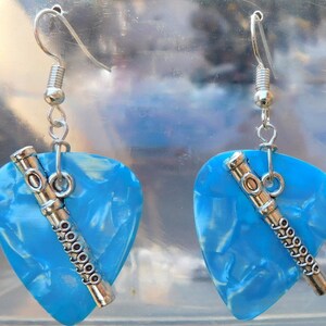 May include: A pair of earrings featuring light blue guitar pick shapes with a silver-colored flute charm. The earrings have a silver-colored hook for pierced ears. The guitar picks have a marbled effect.