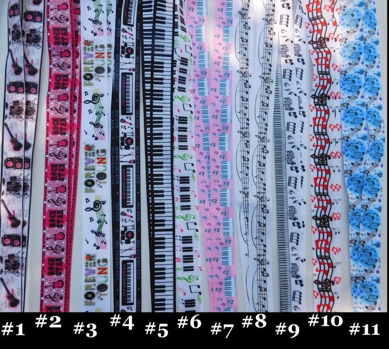 May include: A collection of eleven lanyards with various musical and rock-and-roll themed designs. The lanyards feature images of guitars, keyboards, musical notes, and the text "ROCK STAR" and "FOREVER YOUNG". The lanyards are in various colors, including black, white, pink, and blue.