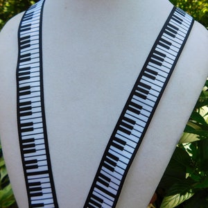 May include: A pair of black and white piano key suspenders. The suspenders are displayed on a white mannequin. The piano key design is printed on a black background. The suspenders are made of a sturdy material.