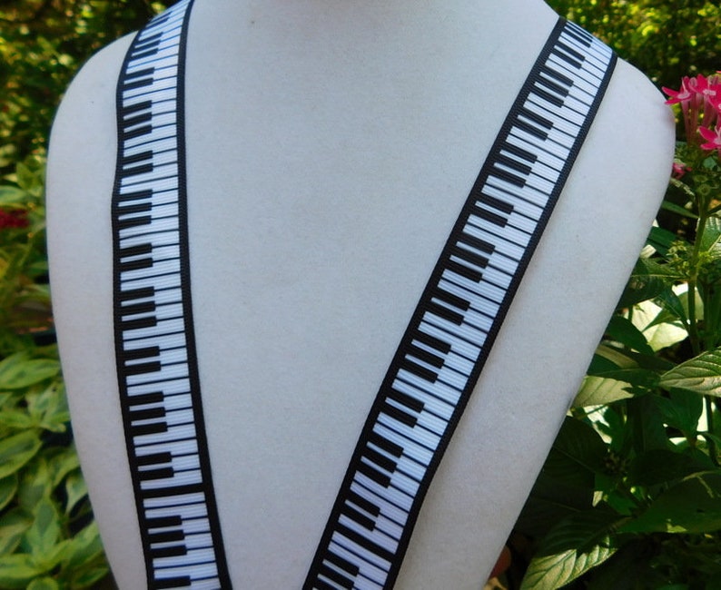 May include: A pair of black and white piano key suspenders. The suspenders are displayed on a white mannequin. The piano key design is printed on a black background. The suspenders are made of a sturdy material.