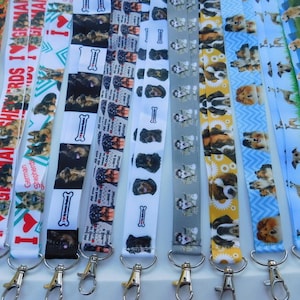 May include: A collection of lanyards with various dog-themed patterns. Designs include German Shepherds, dog bones, and other dog breeds. Each lanyard has a metal clasp.