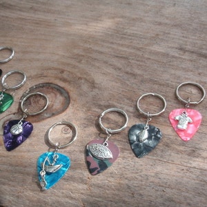 May include: A selection of guitar pick keyrings with sports-themed charms. The picks are in various colours, including red, black, green, purple, blue, pink, and camouflage. Charms include a golf club, basketball, football, and baseball glove.