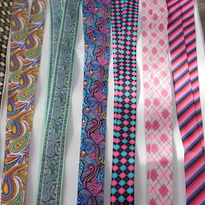 May include: Assortment of eight different patterned ribbon trims. The ribbons are all 1 inch wide and feature various colors and designs, including paisley, geometric, and floral patterns.