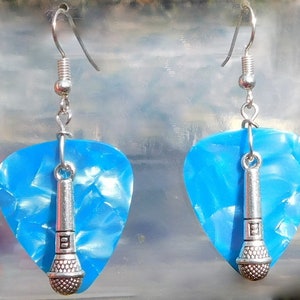 May include: A pair of handmade earrings featuring blue guitar picks with a pearlescent finish. Each earring has a silver-colored microphone charm suspended from a silver-tone ear wire. The earrings are designed for music lovers.