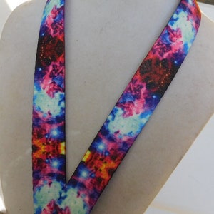 May include: A lanyard with a vibrant galaxy print. The design features a colorful mix of blues, pinks, reds, and yellows, creating a cosmic effect. The lanyard is made of a durable material and is designed to be worn around the neck.