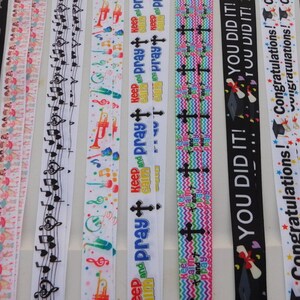 May include: Assortment of black and white ribbon with various designs, including music notes, dancing figures, graduation caps, and the text "Keep and Pray".