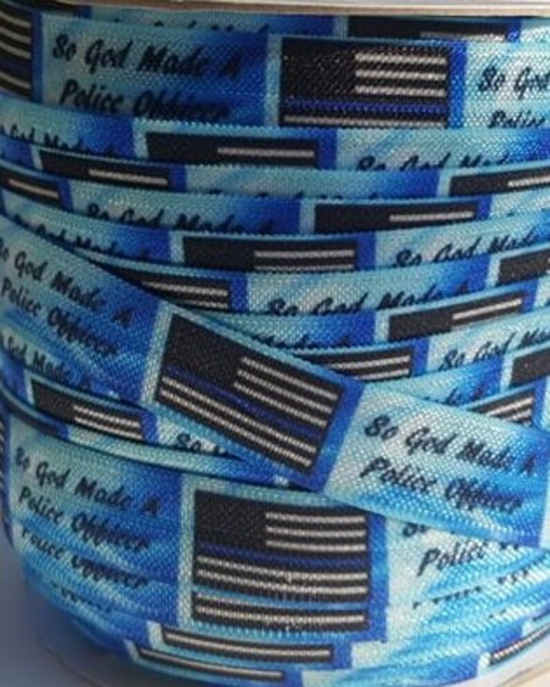 May include: A roll of blue and white ribbon with a thin black line. The ribbon has a repeating pattern of a thin blue line American flag and the text "So God Made A Police Officer".