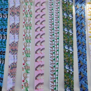 May include: A collection of colorful lanyards with various patterns. Designs include foxes, pandas, sloths, hedgehogs, birds, bees, and floral motifs. The lanyards are made of a smooth, ribbon-like material and are displayed vertically.