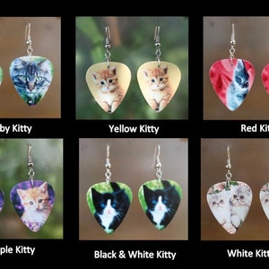 May include: A collection of six pairs of earrings, each featuring a different cat image on a guitar pick shape. The earrings are labeled "Tabby Kitty", "Yellow Kitty", "Red Kitty", "Purple Kitty", "Black & White Kitty", and "White Kitties".
