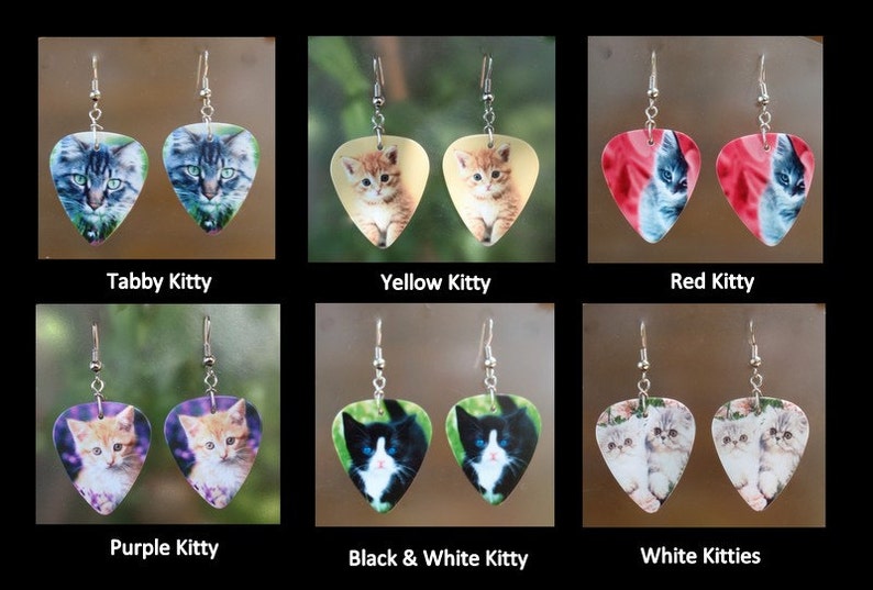 May include: A collection of six pairs of earrings, each featuring a different cat image on a guitar pick shape. The earrings are labeled "Tabby Kitty", "Yellow Kitty", "Red Kitty", "Purple Kitty", "Black & White Kitty", and "White Kitties".