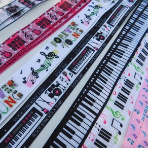 May include: A collection of musical-themed ribbons in various designs. Ribbons feature musical notes, piano keys, guitars, and the text "ROCK STAR" and "FOREVER YOUNG". Colors include pink, black, white, and green. Ideal for crafting or music-related projects.